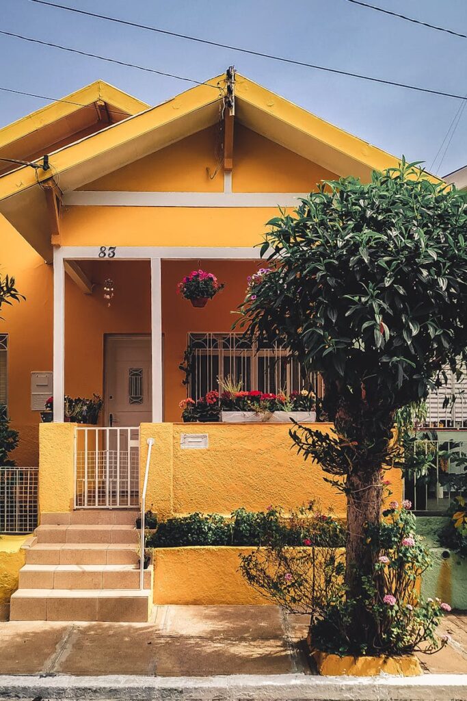Bright yellow house with lush garden, vibrant flowers, and welcoming porch entrance.